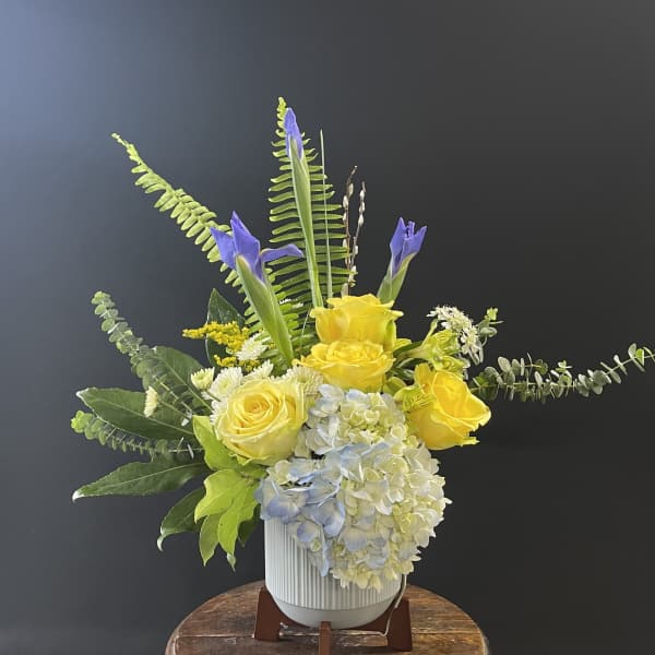 Yellow roses and blue hydrangea in a white vase with tall purple iris