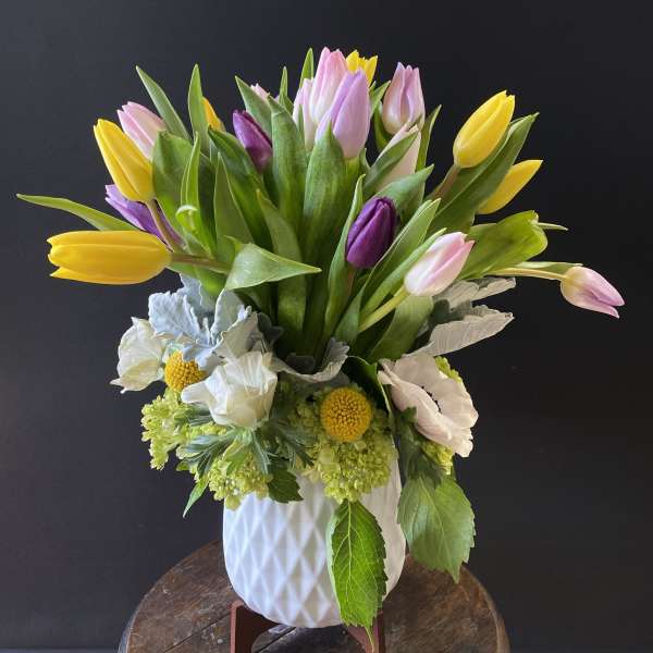 Bouquet of yellow, pink, and purple tulips in a white vase