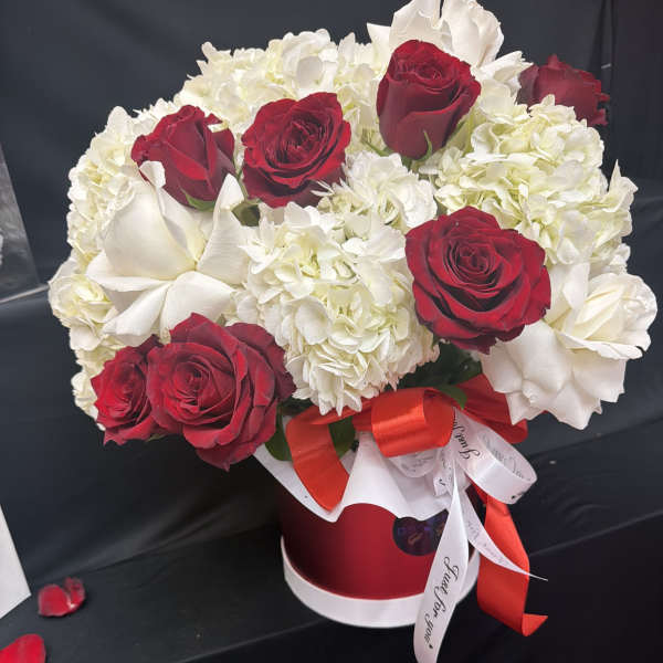 Red roses and white hydrangeas arranged in a red hatbox with ribbon