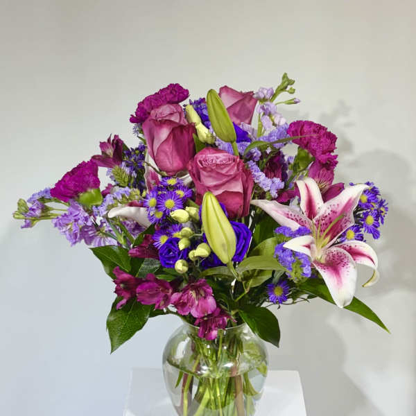 Bouquet of pink roses, lilies, and purple flowers in a glass vase