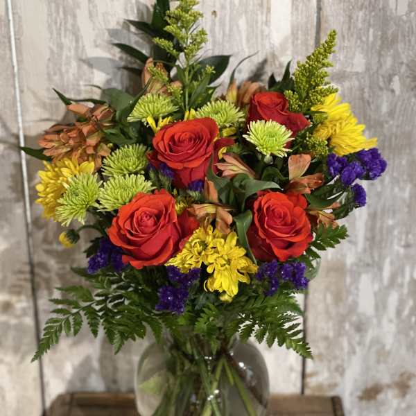 Mixed bouquet of red roses, yellow chrysanthemums, and purple filler in a glass vase