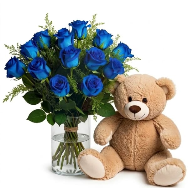 Blue roses in a glass vase beside a beige teddy bear