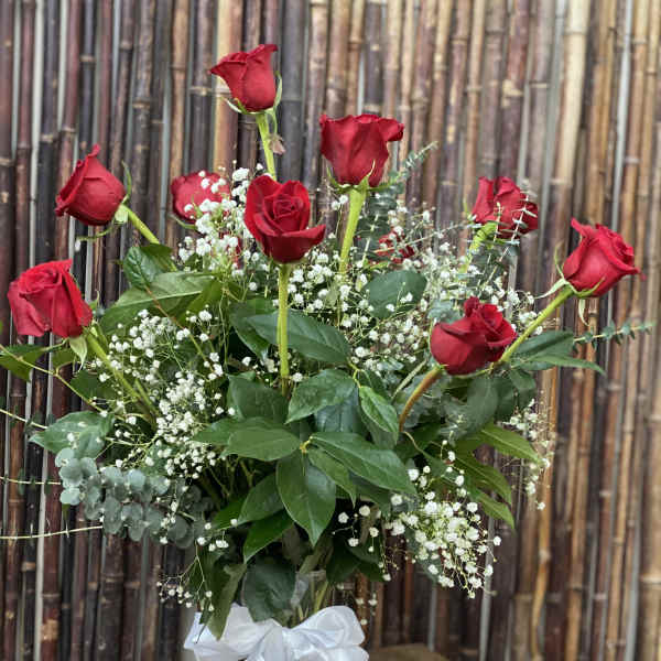 Red roses in a glass vase with baby's breath and a white ribbon