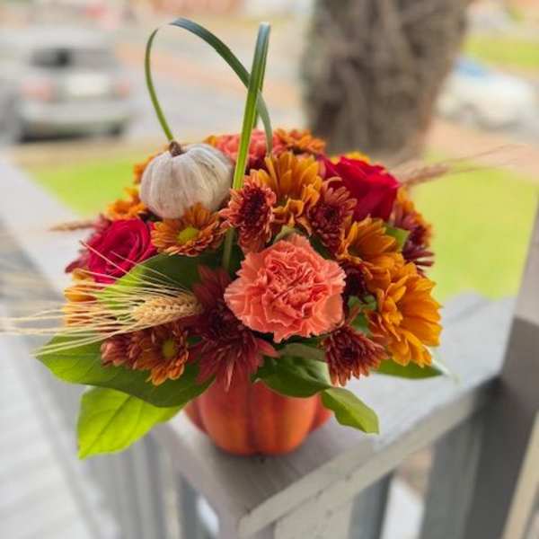 Orange and red mixed flower arrangement in a small pumpkin-shaped container