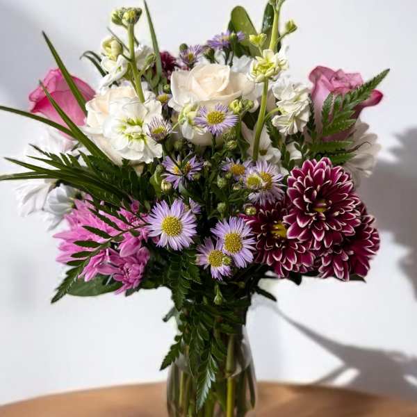 Mixed bouquet of white, pink, and purple flowers in a clear glass vase
