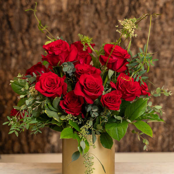 Arrangement of red roses in a gold cylinder vase on a marble surface