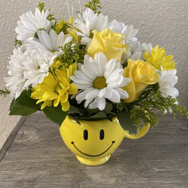 Yellow and white flowers arranged in a smiley-face mug