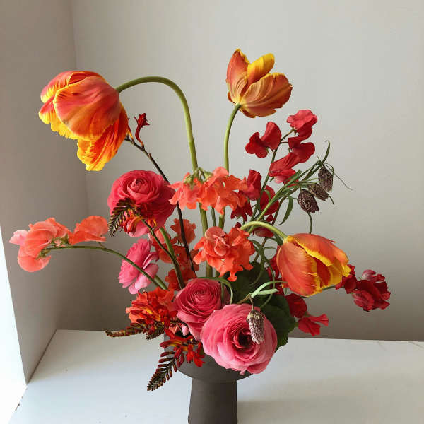 Bright mixed bouquet in a dark vase with orange tulips and pink ranunculus
