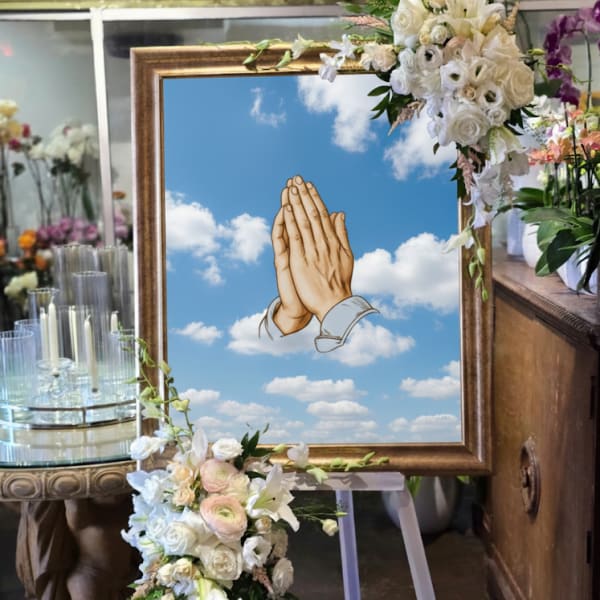 Floral funeral easel with white flowers and a framed praying hands tribute