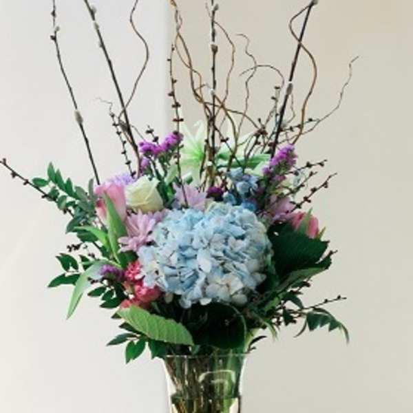 Tall floral arrangement with blue hydrangea in a glass vase