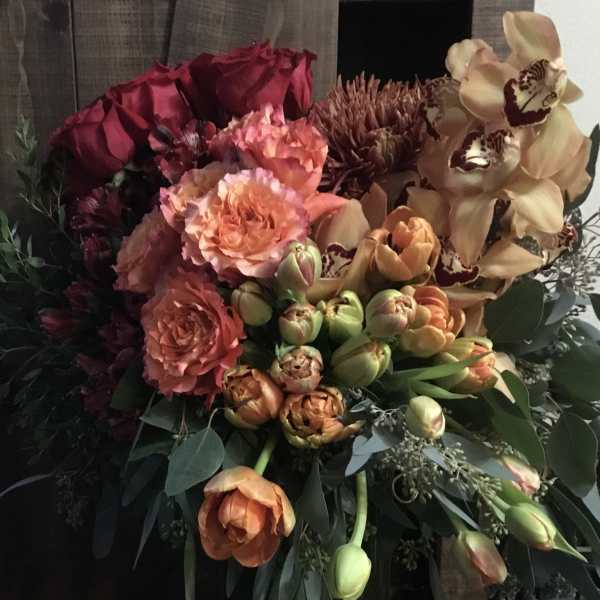 Bouquet of roses, tulips, and orchids in a tall green vase