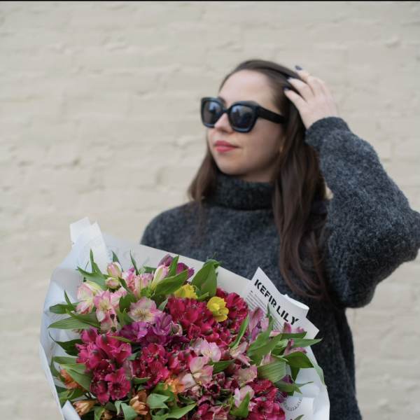 Woman holding a large bouquet of pink and magenta flowers wrapped in white paper