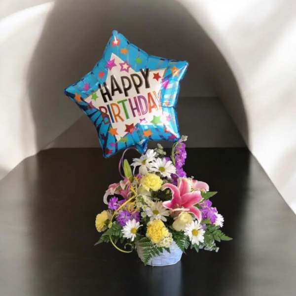 Birthday balloon above a small mixed flower arrangement in a basket