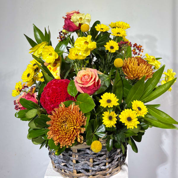 Mixed bouquet in a woven basket with yellow, pink, and orange flowers