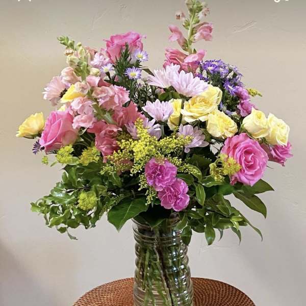 Mixed pink, yellow, and purple flowers in a clear glass vase
