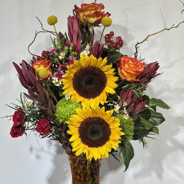 Sunflowers and roses arranged in a tall amber glass vase