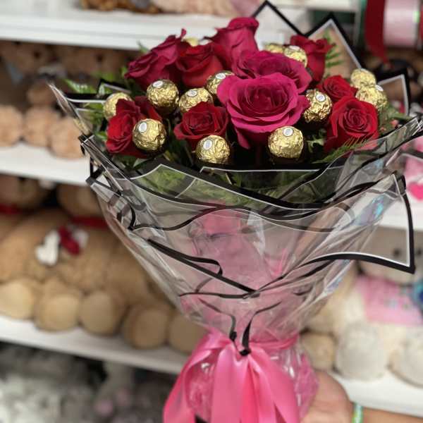 Bouquet of red roses and gold-wrapped chocolates in clear wrap with a pink ribbon