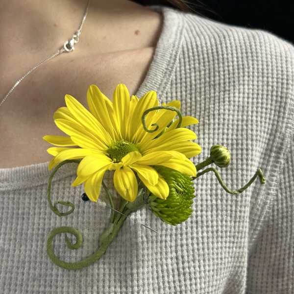 Yellow daisy boutonniere pinned to a sweater