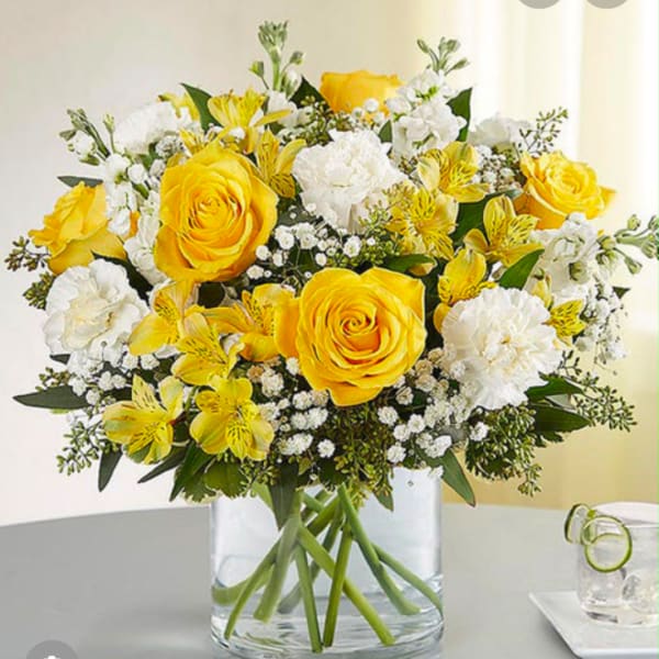 Yellow roses and white flowers in a clear glass vase