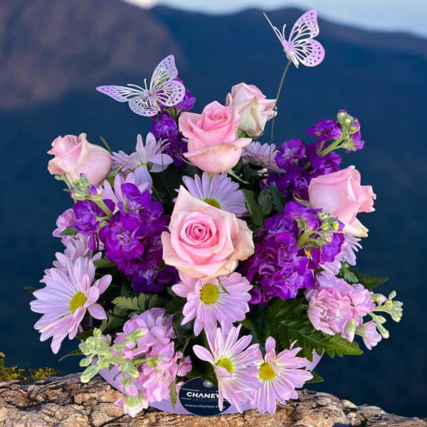 Pink roses and lavender daisies in a round bouquet with butterfly picks