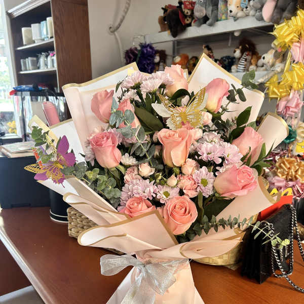 Pink rose bouquet with small daisies wrapped in pale paper and a silver bow