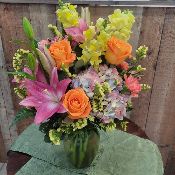 Colorful bouquet of lilies, roses, and hydrangeas in a green glass vase