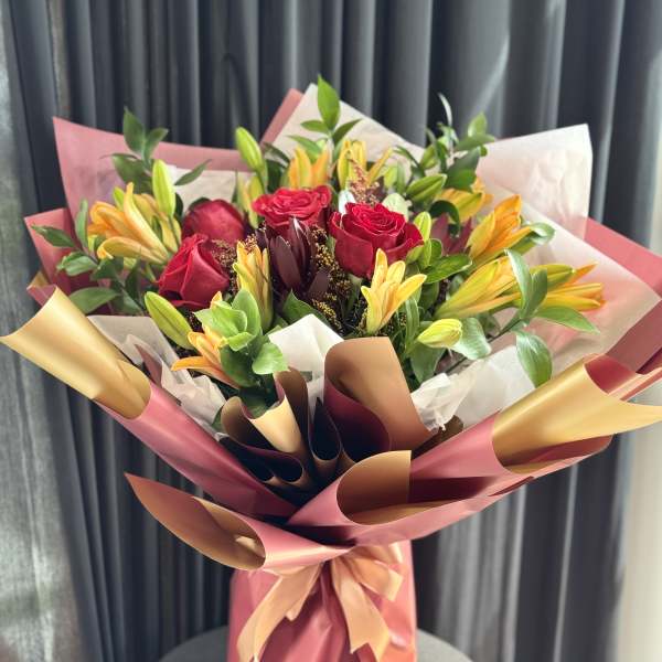 Bouquet of red roses and yellow lilies wrapped in pink paper