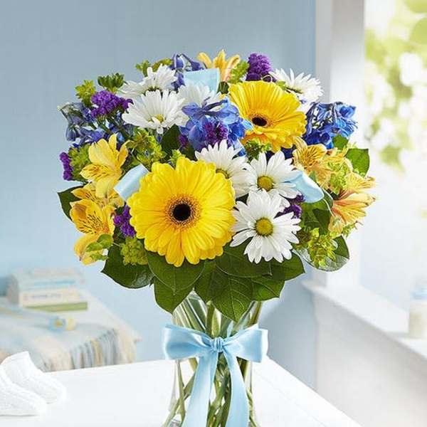Bouquet of yellow gerbera daisies, white daisies, and blue flowers in a glass vase