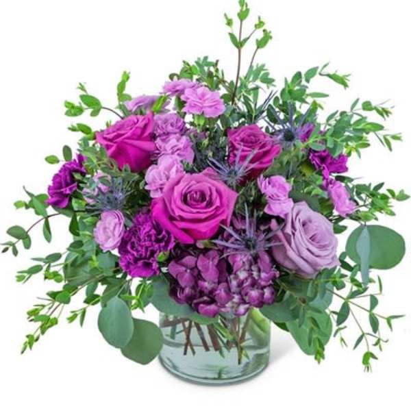 Purple roses and carnations in a glass vase with greenery
