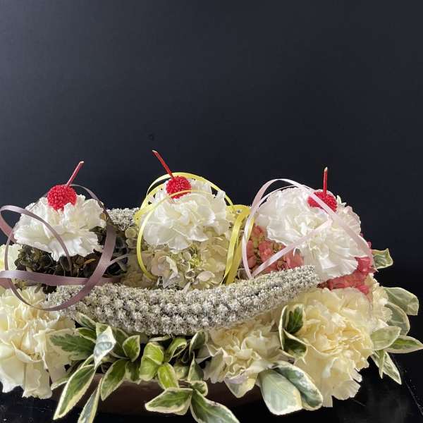 Three small floral arrangements with white blooms and ribbon loops on a dark background