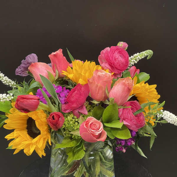 Colorful mixed bouquet with sunflowers, pink roses, and tulips in a glass vase