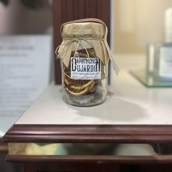 Glass apothecary jar with dried orange slices and a paper-wrapped lid on a wooden shelf.