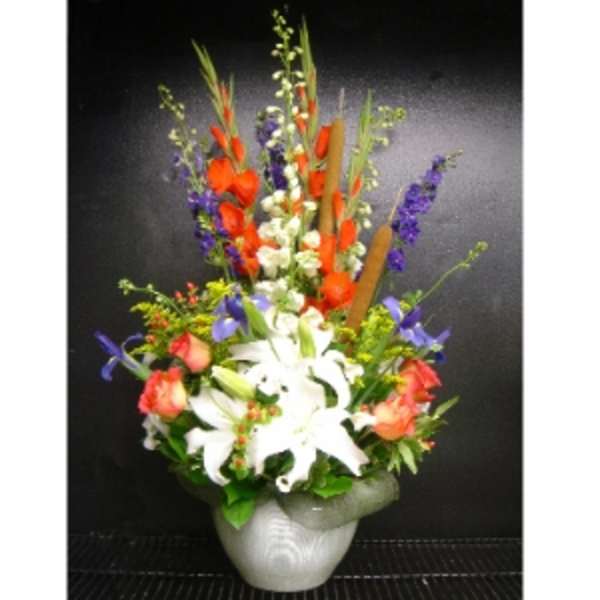 Tall mixed arrangement with white lilies and bright orange and purple flowers in a light gray urn-style vase