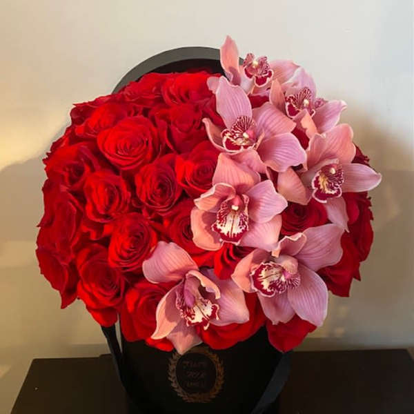 Red roses and pink orchids arranged in a black hatbox