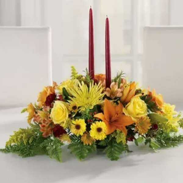 Low floral centerpiece with two red taper candles and orange-yellow blooms