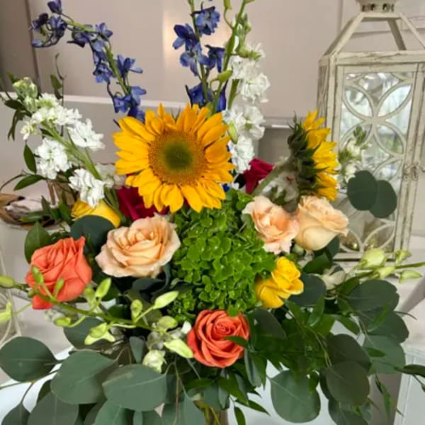 Mixed bouquet with sunflowers, roses, and blue flowers in a glass vase