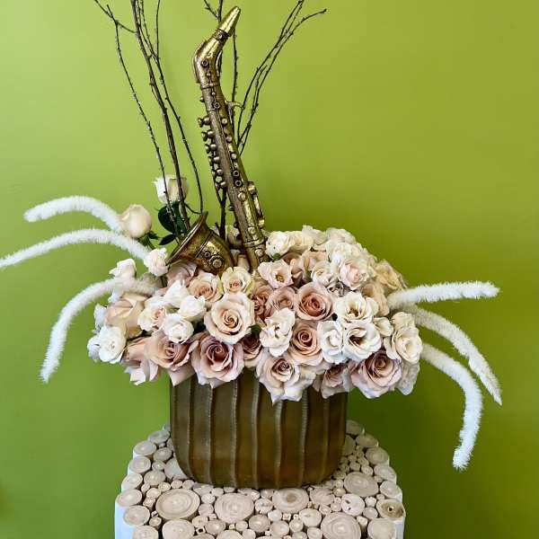 Arrangement of pale roses with a gold saxophone decoration in a brown vase