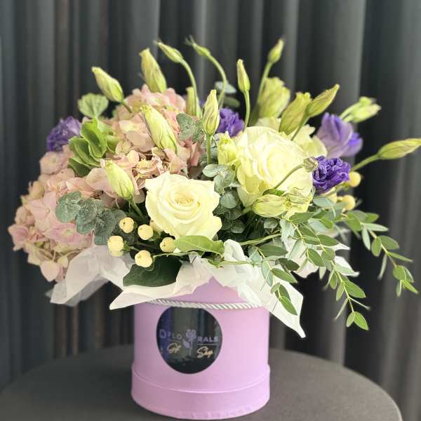 Bouquet of pale pink hydrangeas, white roses, and purple blooms in a pink box