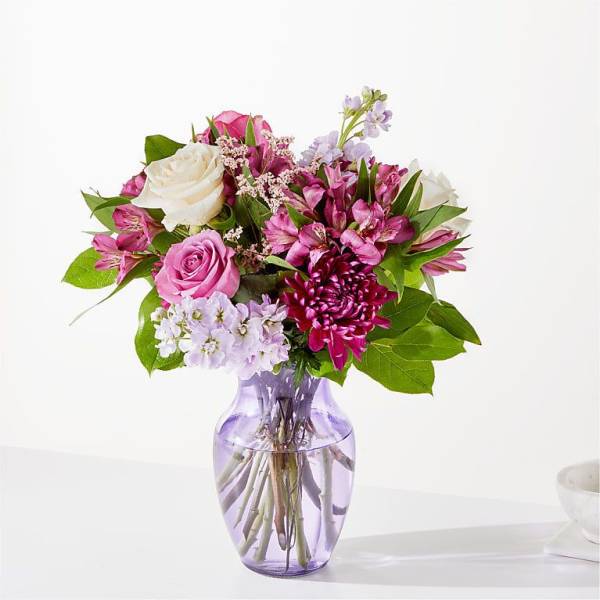 Pink and white mixed flower bouquet in a purple glass vase