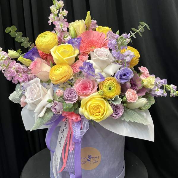 Mixed bouquet of roses, ranunculus, and lisianthus in a round hat box