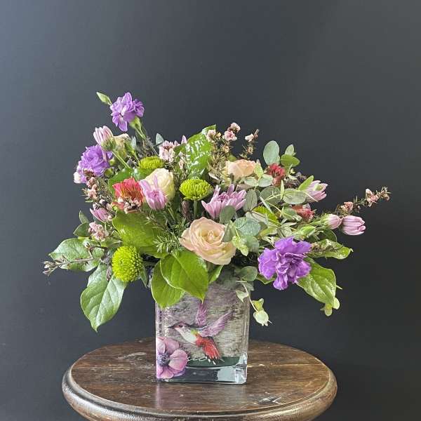 Mixed bouquet in a square glass vase with purple, pink, and green blooms