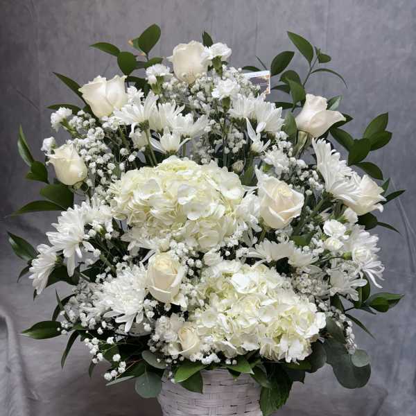 White floral arrangement in a woven basket with roses, hydrangeas, and daisies
