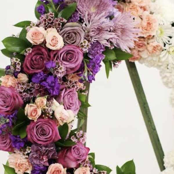 Standing wreath of pink and purple roses, carnations, and mums on an easel.