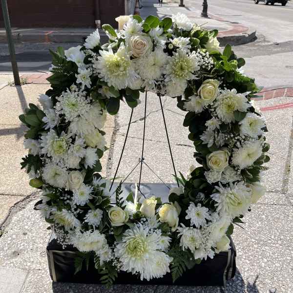 White floral wreath on a stand with roses and daisies
