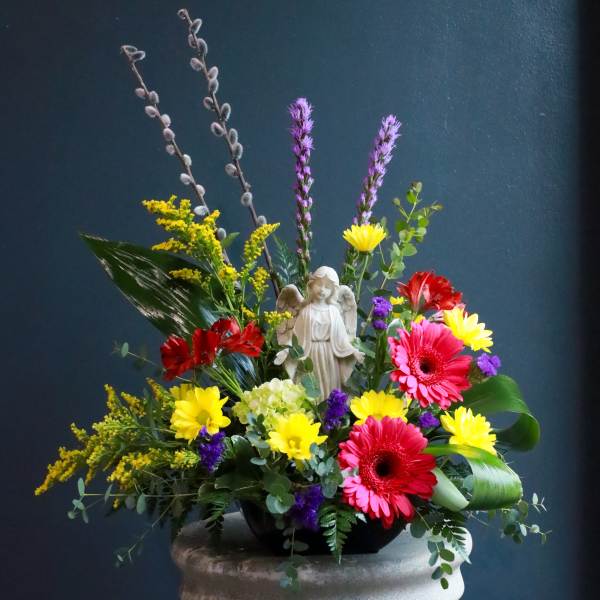 Colorful floral arrangement with an angel figurine in a low black bowl