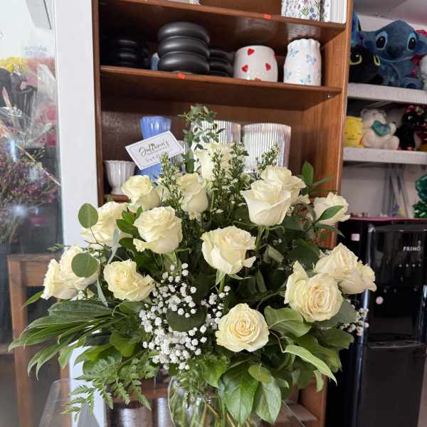 Cream rose arrangement in a glass vase with baby's breath and greenery