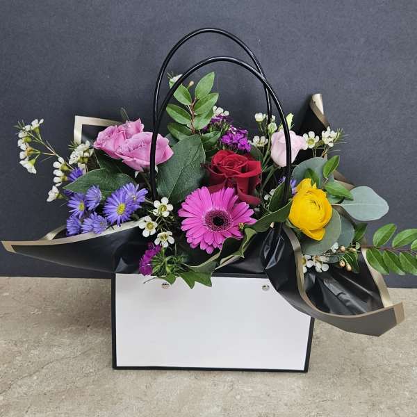 Mixed bouquet in a black handled gift bag with pink, red, yellow, and purple flowers
