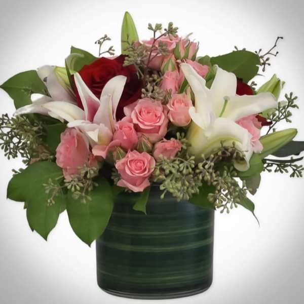 Pink and white roses with lilies in a dark green vase