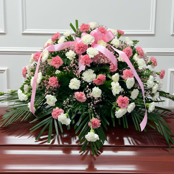 Pink and white carnation spray with a pink ribbon on a casket