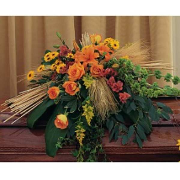 Autumn casket spray with orange roses, lilies, yellow daisies, and wheat on a wooden casket